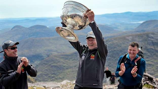Legendary GAA Commentator Mícheál Ó Muircheartaigh lifts the Sam Maguire Cup on the Summit of Carrauntoohil, MacGillycuddy's Reeks, Kerry, with programme director and former Galway star Alan Kerins, left, during the 'Sam to Summit' in aid of the Alan Kerins Project which saw Sam Maguire and representatives and players with All-Ireland football medals from each of the 32 counties reach the top of Ireland’s highest mountain at Carrauntoohil in Kerry. Photo by Valerie O'Sullivan/Sportsfile.