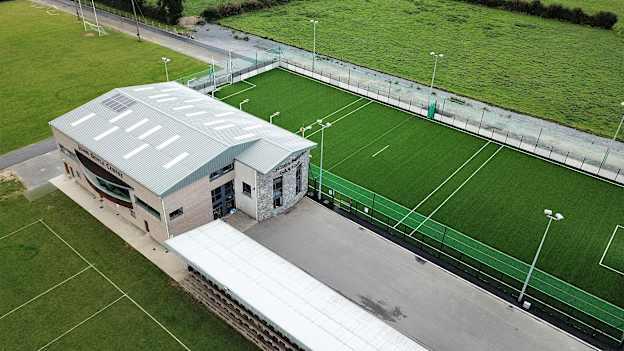 An aerial view of Holycross-Ballycahill GAA club's facilities including the John Doyle Centre, two grass pitches, and floodlit astro-pitch. 
